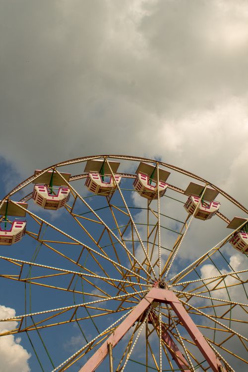 Free Low angle view of a vintage Ferris wheel with a cloudy sky backdrop, offering a nostalgic amusement ride experience. Stock Photo