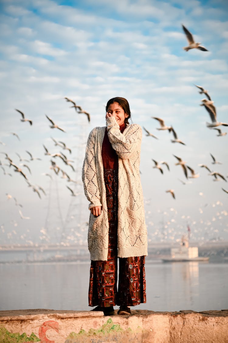 Woman Standing On Ledge In Front Of Flying Birds