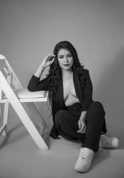 Portrait of a woman in a stylish blazer posing confidently in a monochrome studio setting.