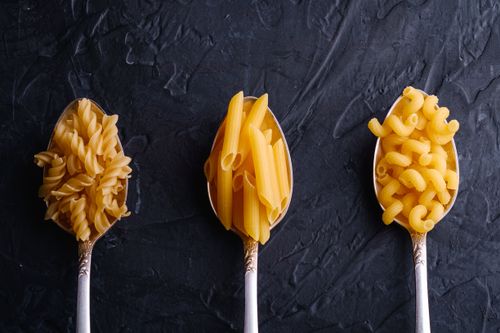 Free Top view of fusilli, penne, and macaroni pasta in silver spoons against a dark background. Stock Photo