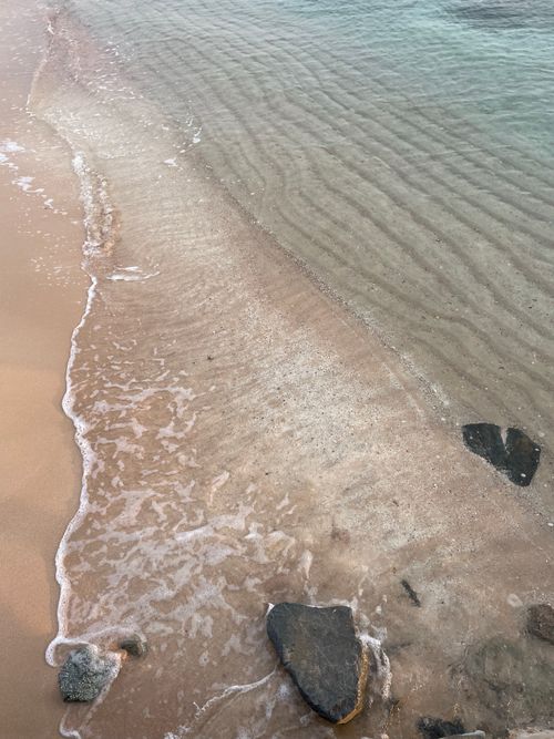 Free Tranquil sandy beach with gentle waves and scattered rocks. Stock Photo