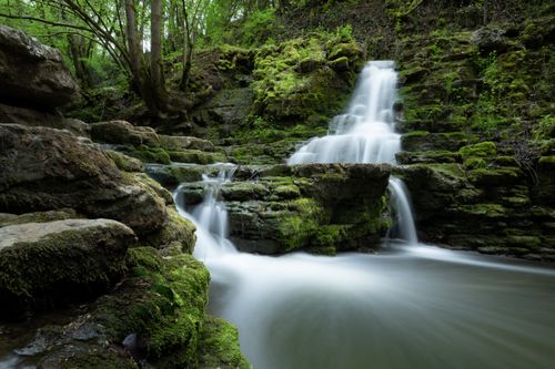 Free A serene waterfall flowing over moss-covered rocks in a lush forest setting, showcasing nature's beauty. Stock Photo
