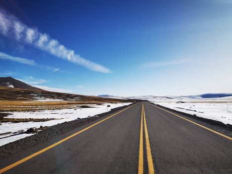 A scenic asphalt road leads through a snowy landscape in Antofagasta, Chile under a clear blue sky.