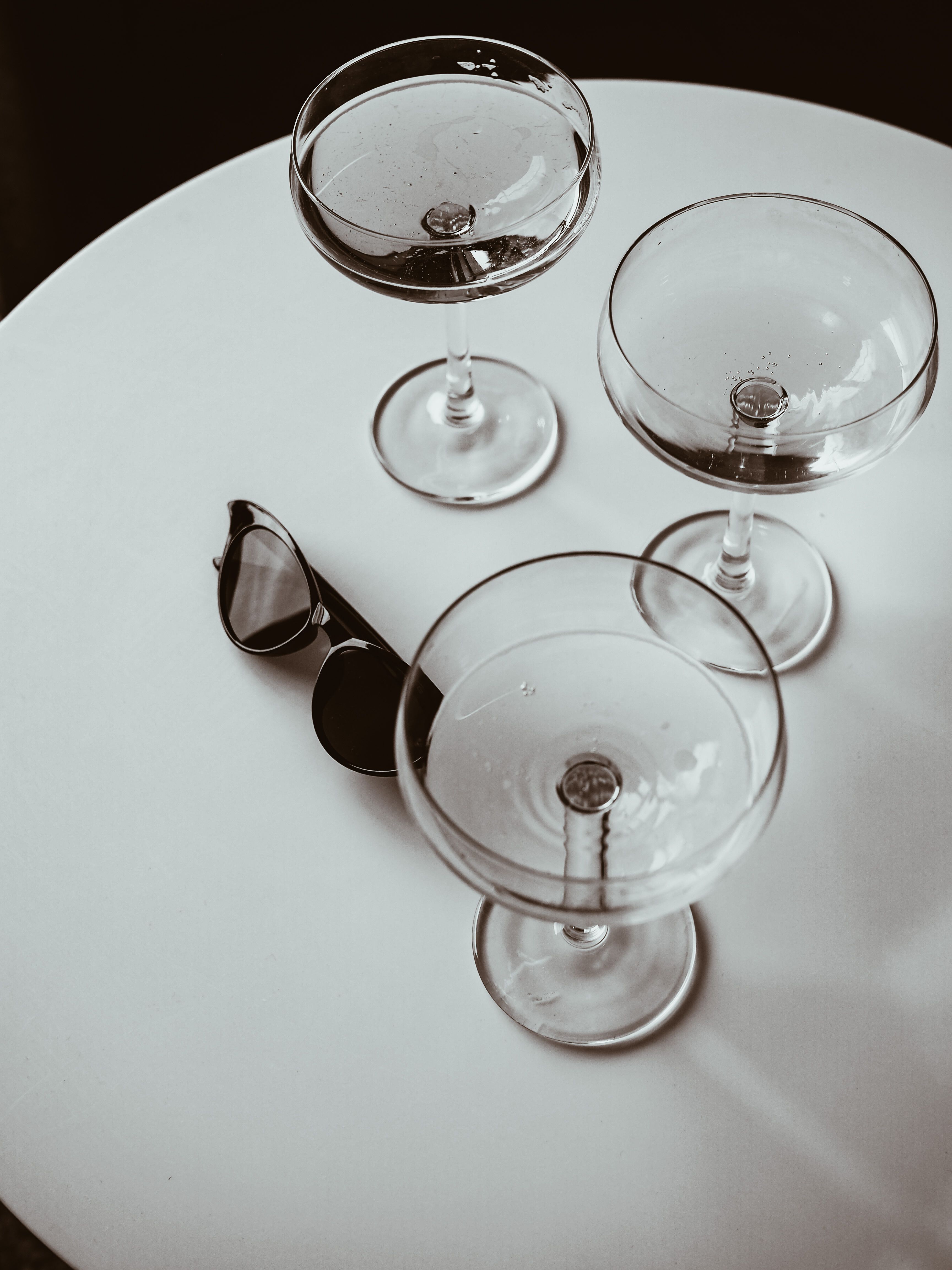 Artistic shot of three empty wine glasses and sunglasses on a white table in Moscow.