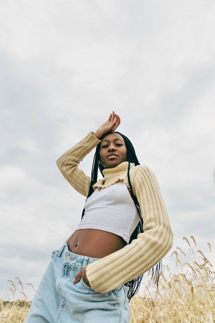 Stylishly dressed woman poses confidently in a Montreal field against a cloudy sky.