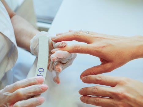 Close-up of a manicurist shaping nails using a file in a salon.