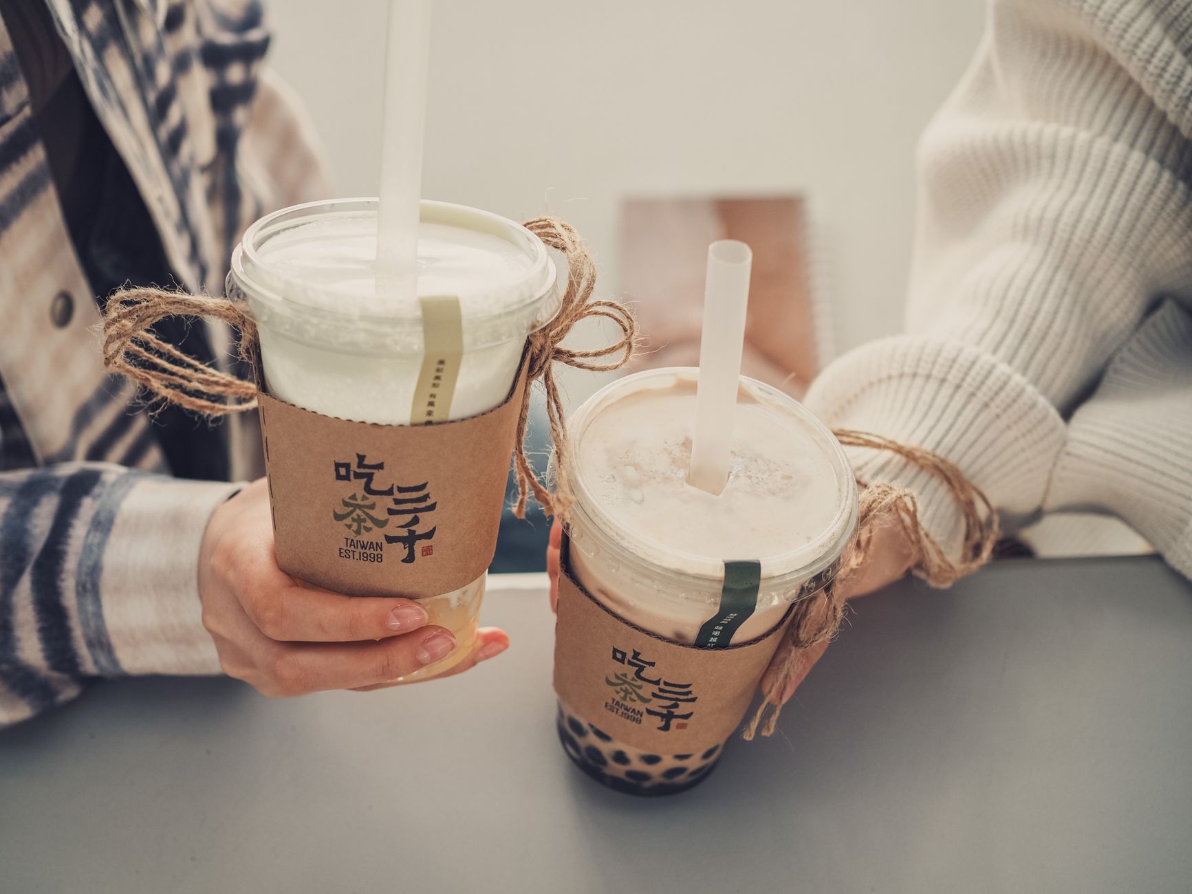 Hands holding bubble tea in plastic cups with decorative holders. Tasty drinks for a cozy moment.