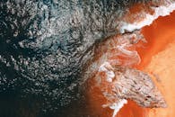 这张航拍照片令人惊叹，捕捉到了充满活力的海岸景象，海浪拍打着岩石与橙色沙滩