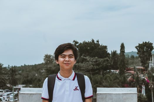 一位年轻的亚洲男子在宿务市的户外微笑着，背景是树木