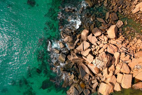 Free Spectacular aerial shot of rocky coastline meeting turquoise ocean waves. Stock Photo