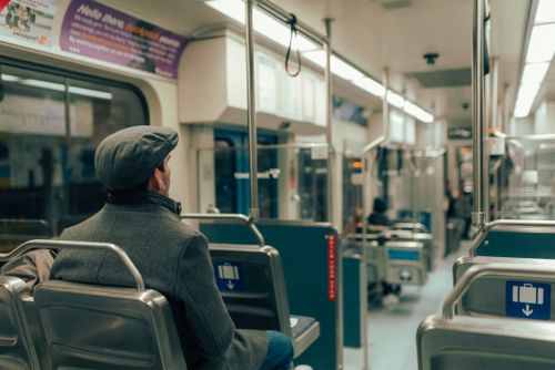 Free A man in a cap and coat sits inside a modern subway train car. Stock Photo