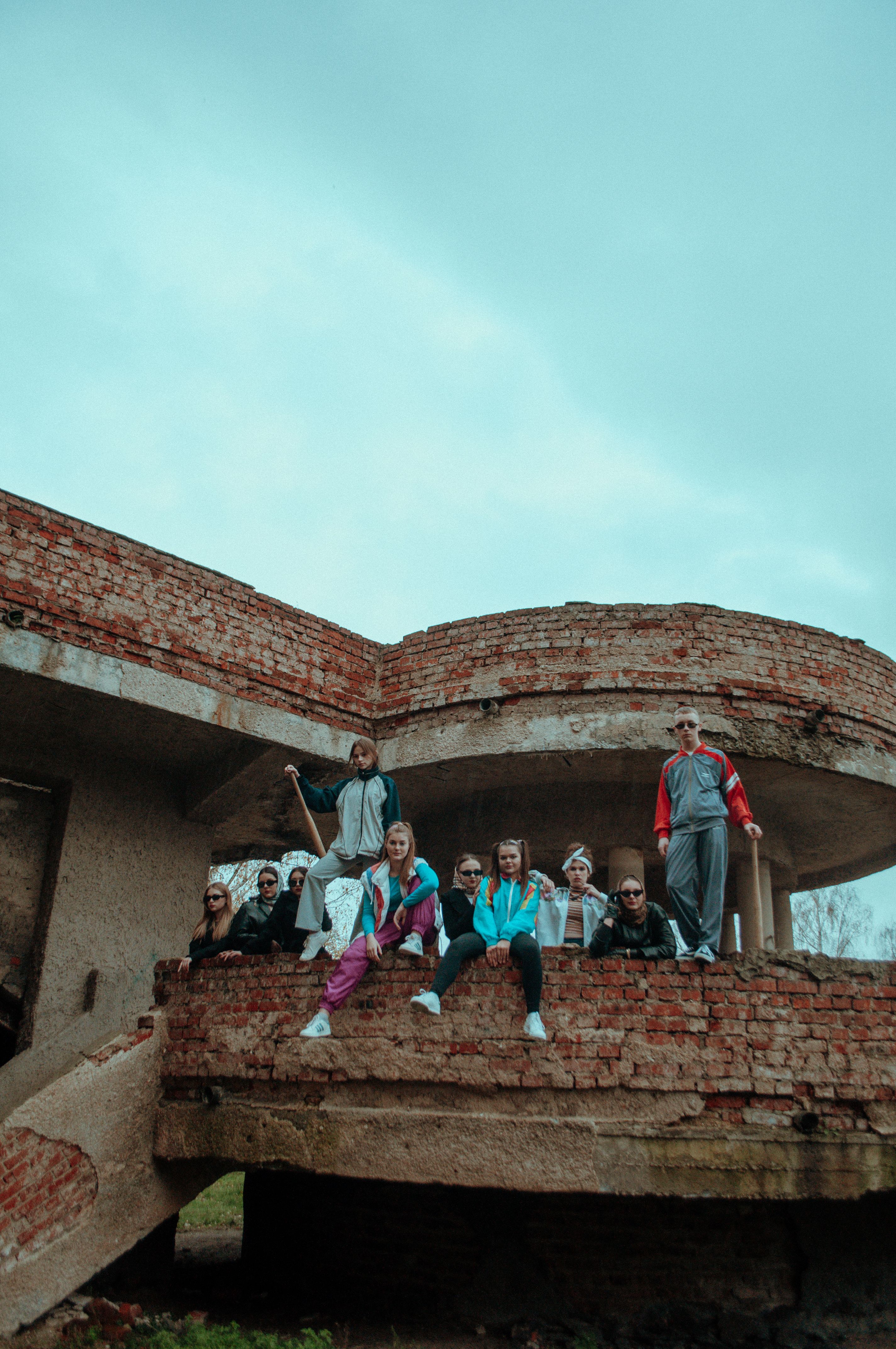 Group of teenagers in casual attire sitting on an abandoned building under a blue sky.