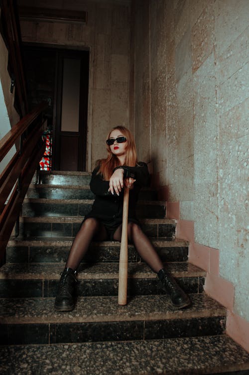 A Woman Sitting on Stairs While Holding a Baseball Bat