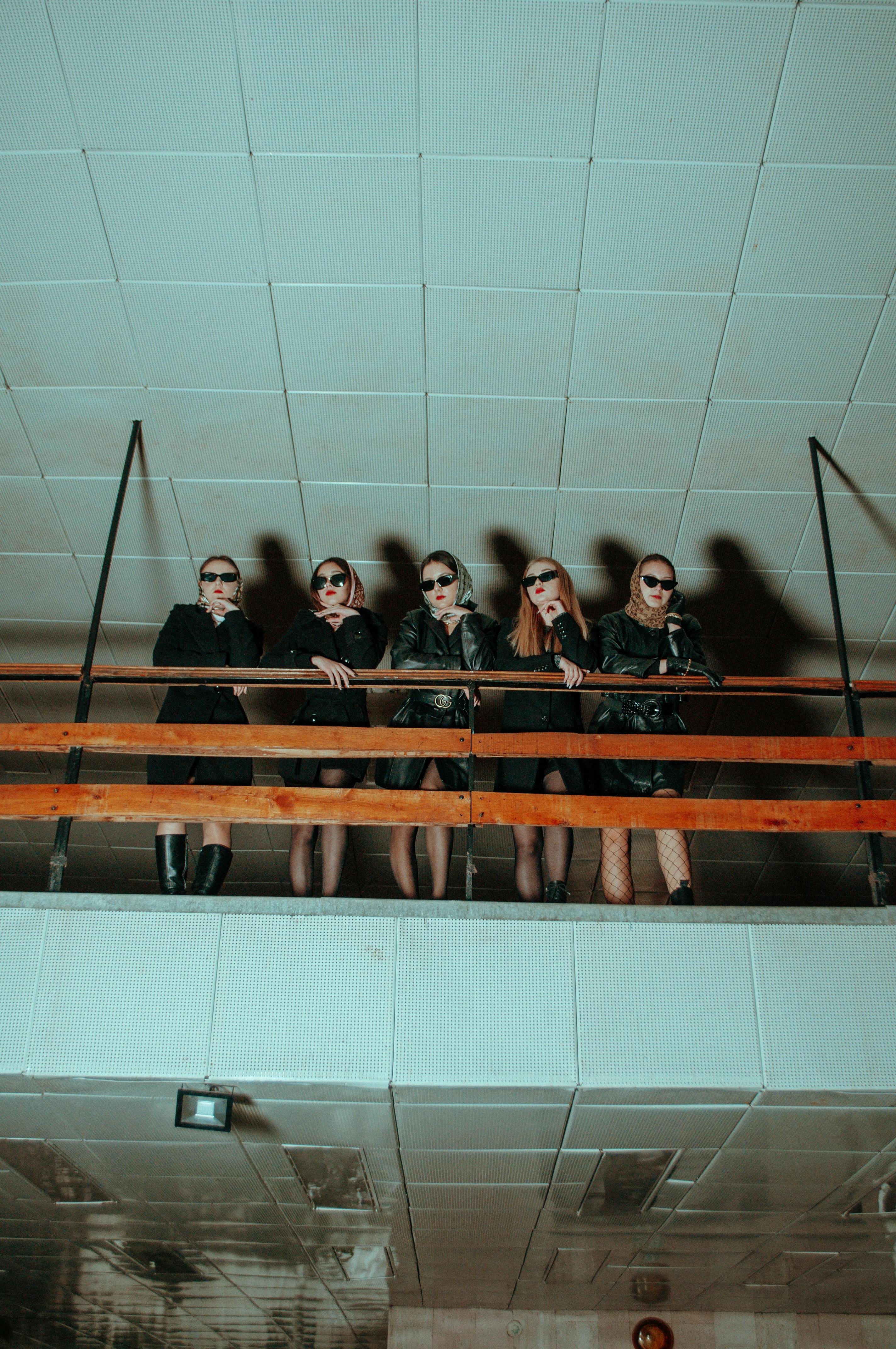 group of young women in black clothes and sunglasses standing on a balcony in a building