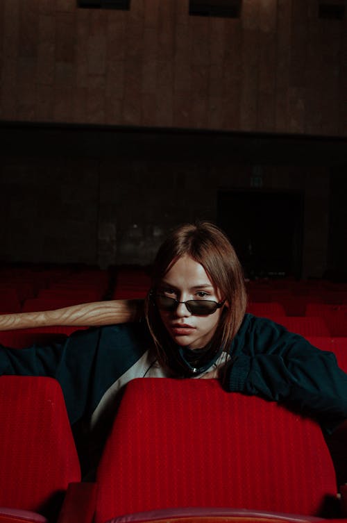 A Girl Wearing Sunglasses and Holding a Baseball Bat Sitting in a Theater