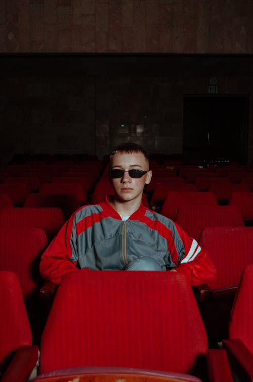 Boy in a Jacket and Sunglasses Sitting Alone Inside a Theater 