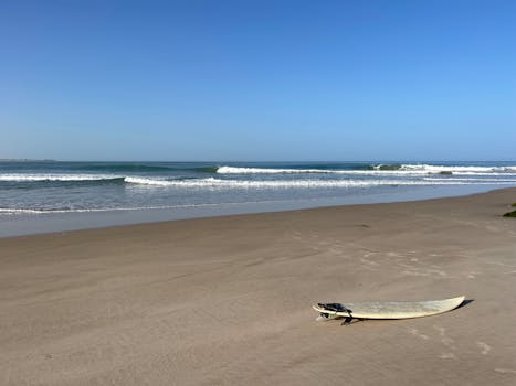 Surfboard on a sandy beach in Dakhla with ocean waves and clear blue sky.