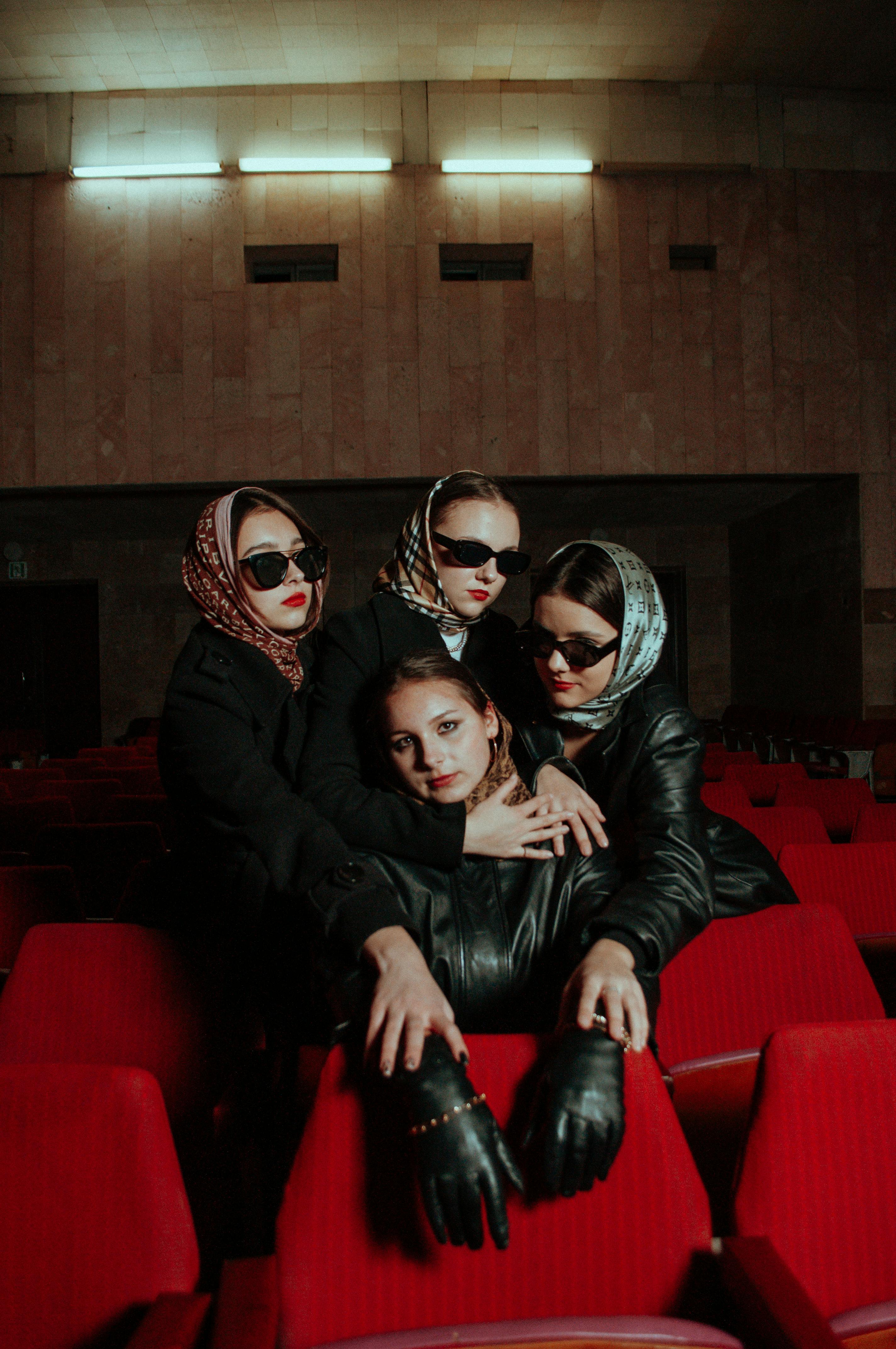 Free Four stylish women in black coats posing in a theater with red seats. Stock Photo