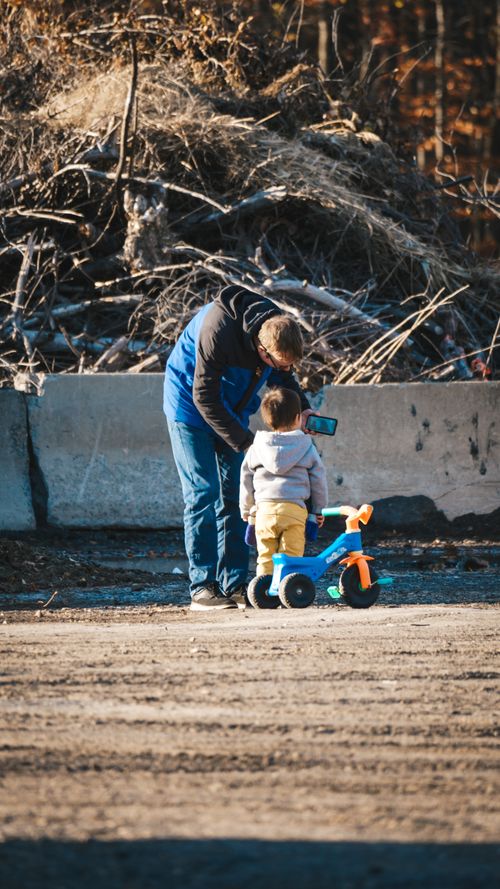 Free Father shares a bonding moment with his child outdoors, capturing memories on a smartphone. Stock Photo