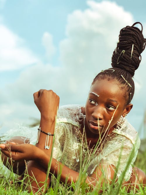 Young Woman with Braided Hair Put Up in a Bun Sitting on a Meadow 