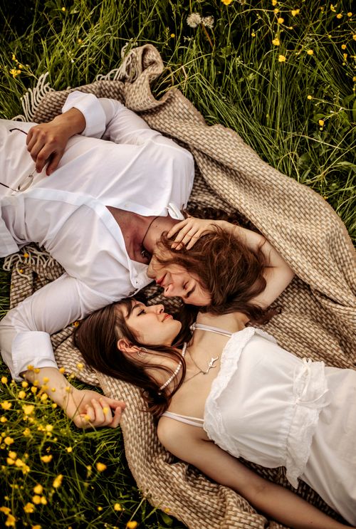 Free A loving couple lies on a blanket in a meadow, surrounded by grass and flowers. Stock Photo