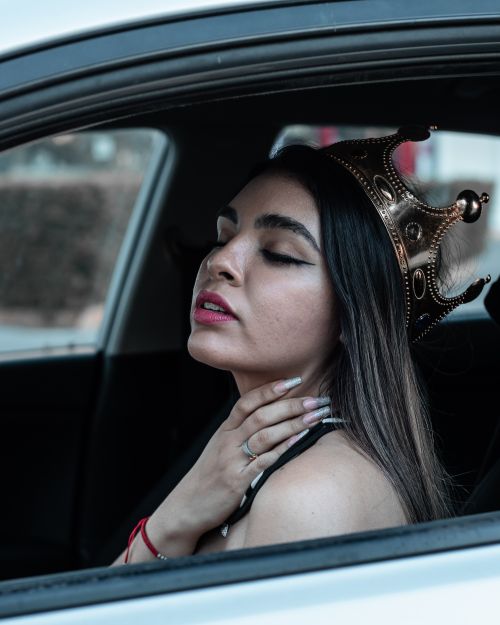 Free Elegant young woman with a crown sitting in a car, showcasing confidence and style. Stock Photo