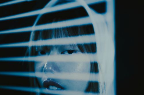 Free Artistic portrait of a woman behind blinds with blue lighting and deep shadows. Stock Photo
