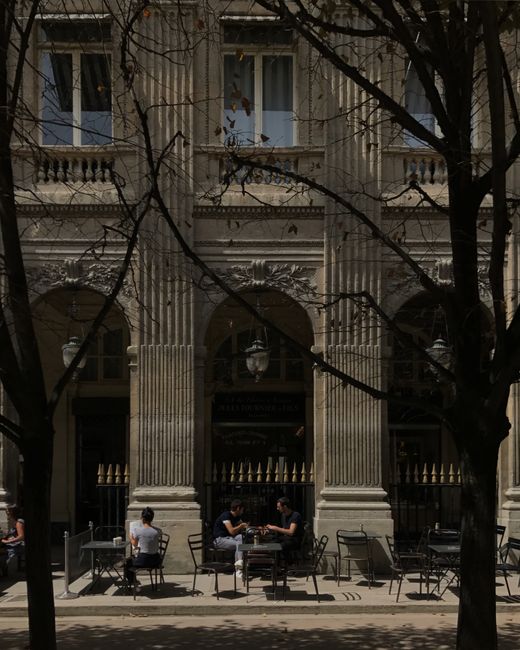 Charming outdoor café with classical architecture facade, people enjoying a sunny day.