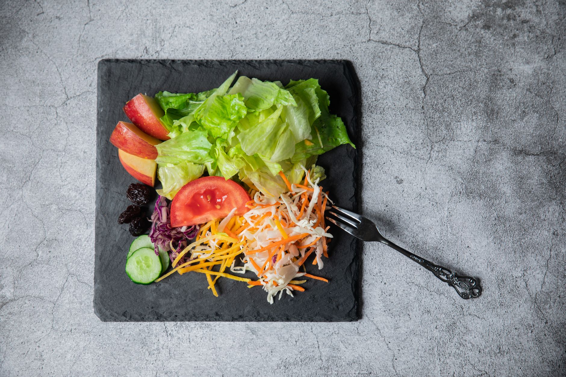 Top view of a colorful vegetable and fruit salad with lettuce, tomato, and apple on a slate plate.