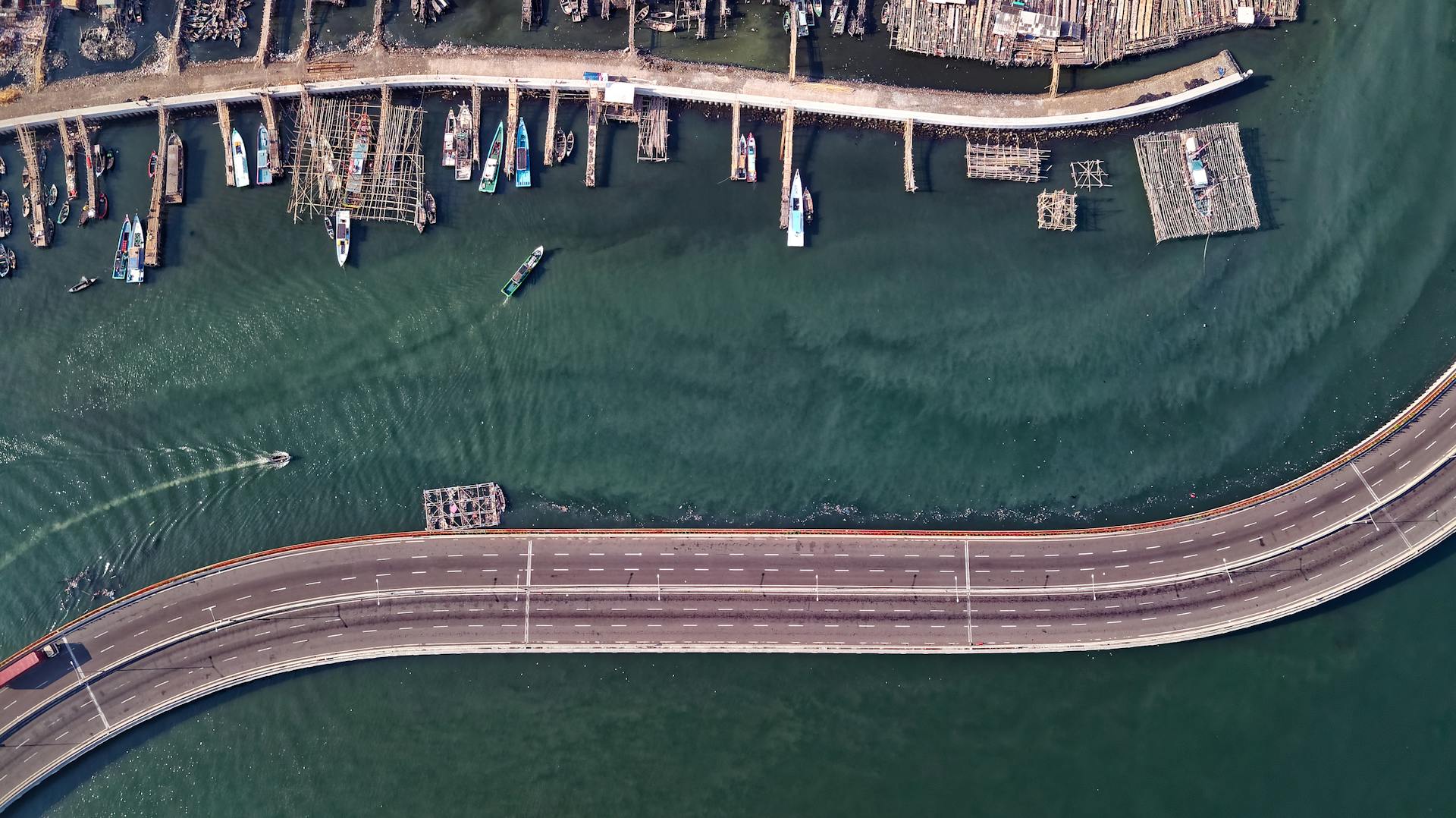 Aerial shot of a curving highway and docks along the Jakarta waterfront with fishing boats.