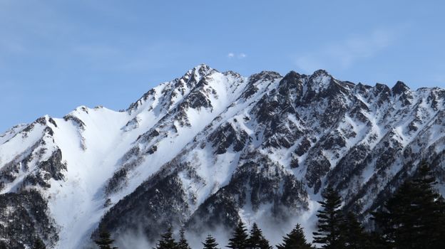Stunning snow-covered rocky mountain peak under a clear blue sky, showcasing winter's beauty.
