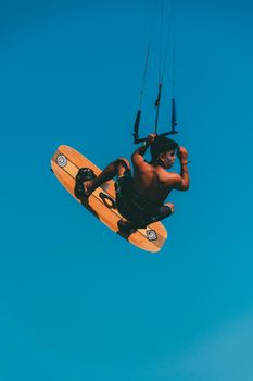 A man performs a skilled kiteboarding trick high in the air against a vibrant blue sky.