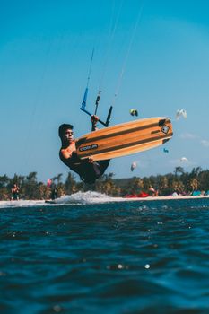A man performs a midair trick while kiteboarding in a tropical beach setting.