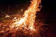 A bright campfire with flames dancing over sticks and twigs at night, creating warmth.