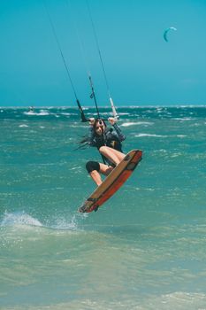 Woman performing a trick midair during kiteboarding on a clear, sunny day.