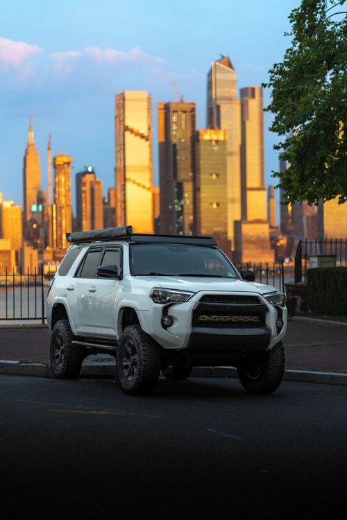 Free A rugged white SUV parked on city streets with a stunning skyline and sunset in the background. Stock Photo