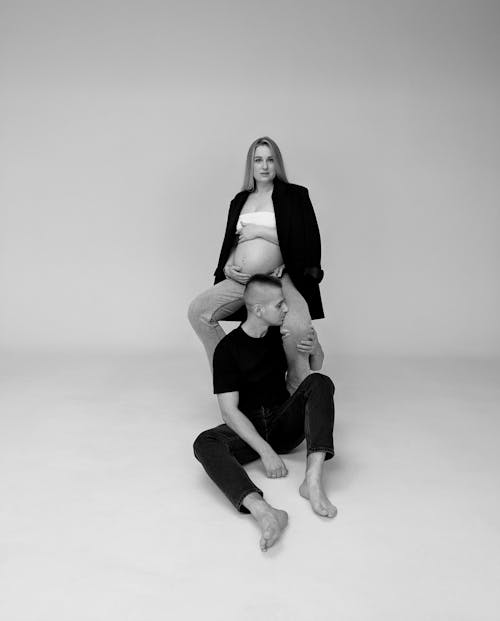 Black and White Photo of Man Sitting in Front of a Pregnant Woman