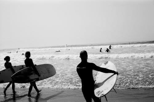 Grayscale Photo of Surfers at the beach 