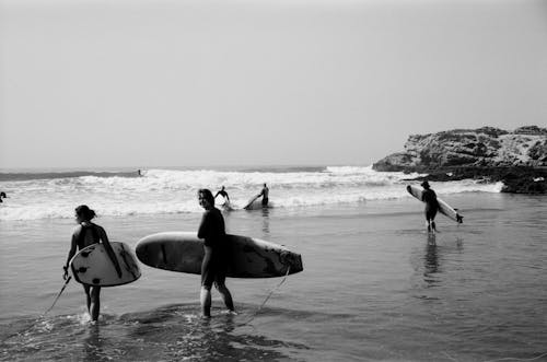 Grayscale Photo of Surfers Walking Towards the Sea