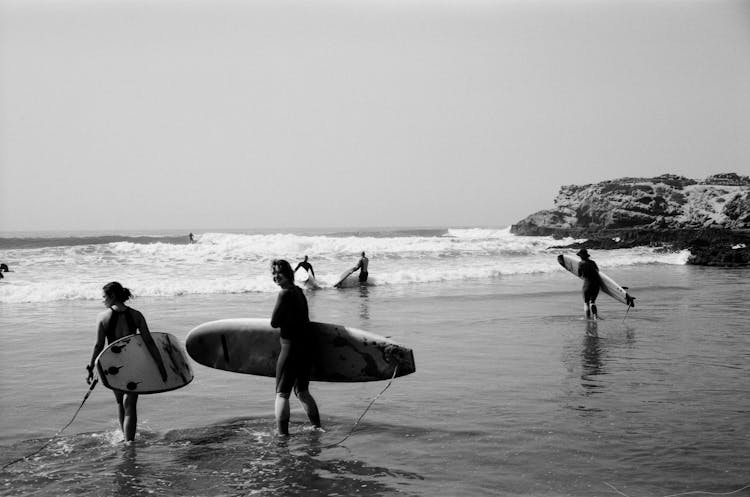 Grayscale Photo Of Surfers Walking Towards The Sea