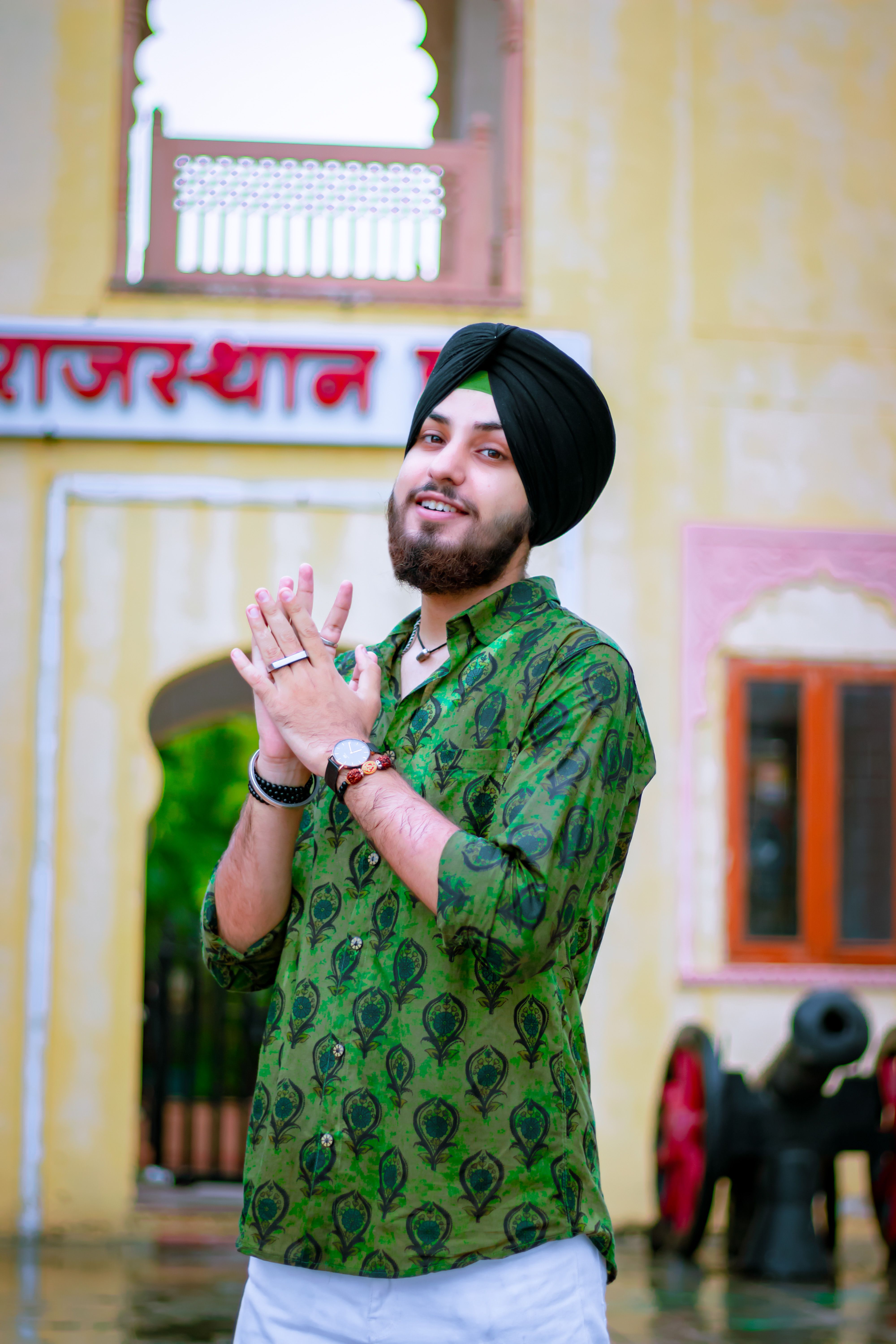 Portrait of a smiling man in a green shirt with a turban, standing at a landmark in Jaipur, India.