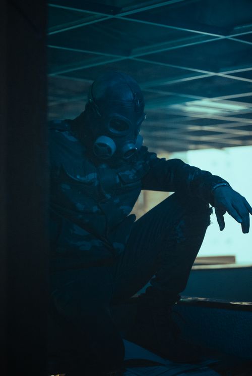 Free A man wearing a gas mask sits in a dimly lit, eerie room creating a sense of mystery and horror. Stock Photo