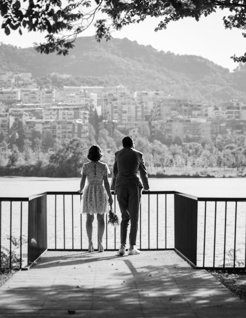 Grayscale Photo of Man and Woman Standing in Front of Railing