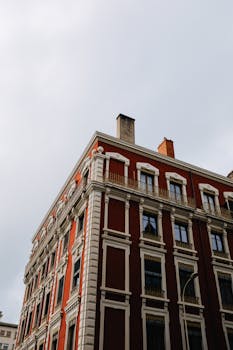 Elegant red tenement building with detailed masonry in an urban setting under a cloudy sky.