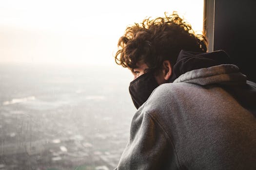 Man in a mask gazing out at sunset cityscape from high-rise window in Chicago, IL.