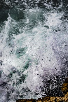 高角度镜头捕捉海浪撞击岩石海岸，产生戏剧性的飞溅效果