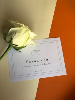 Elegant thank you note with a white rose on a vibrant orange and cream background.