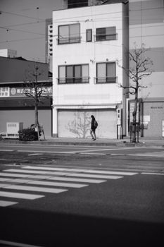 Black and white street photo of a person walking past city buildings.