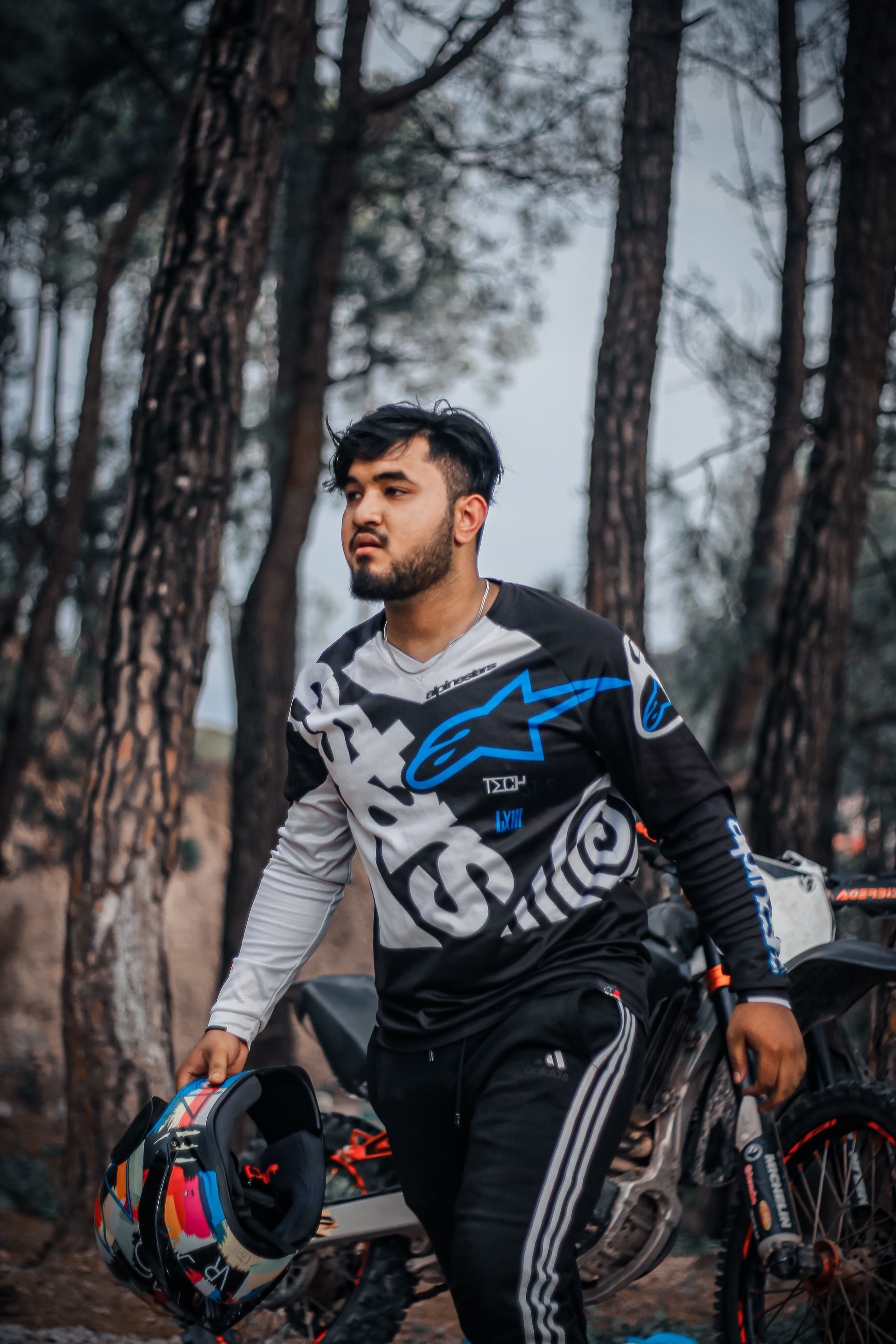 Man walking in forest with motorcycle helmet, surrounded by trees.