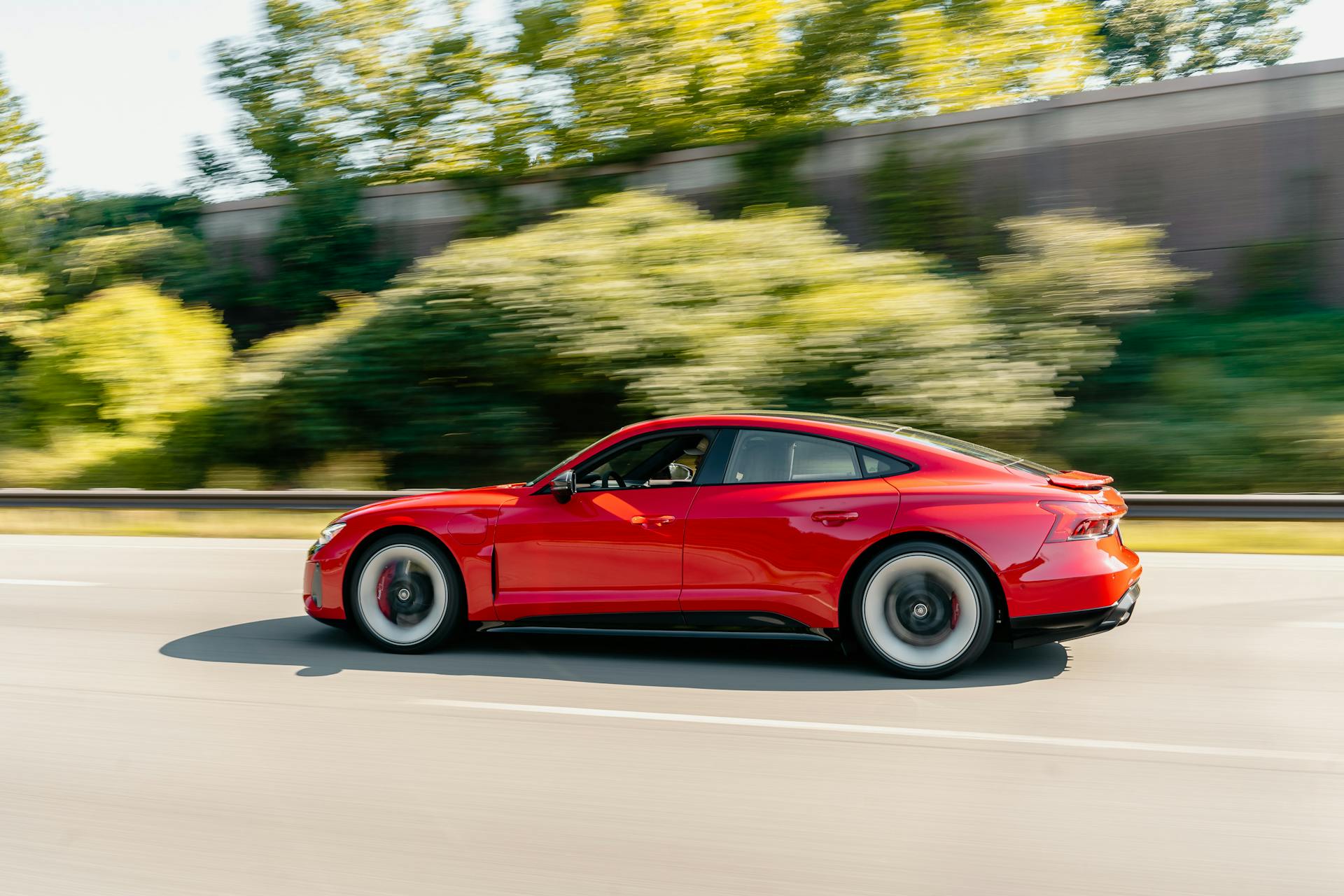 Red electric car speeding on a highway with blurred green trees in the background. Modern transportation concept.